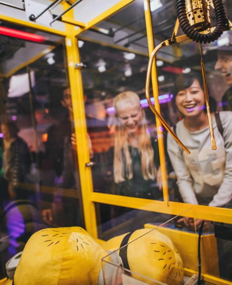 Happy young woman playing toy grabbing game with friends at amusement park.
